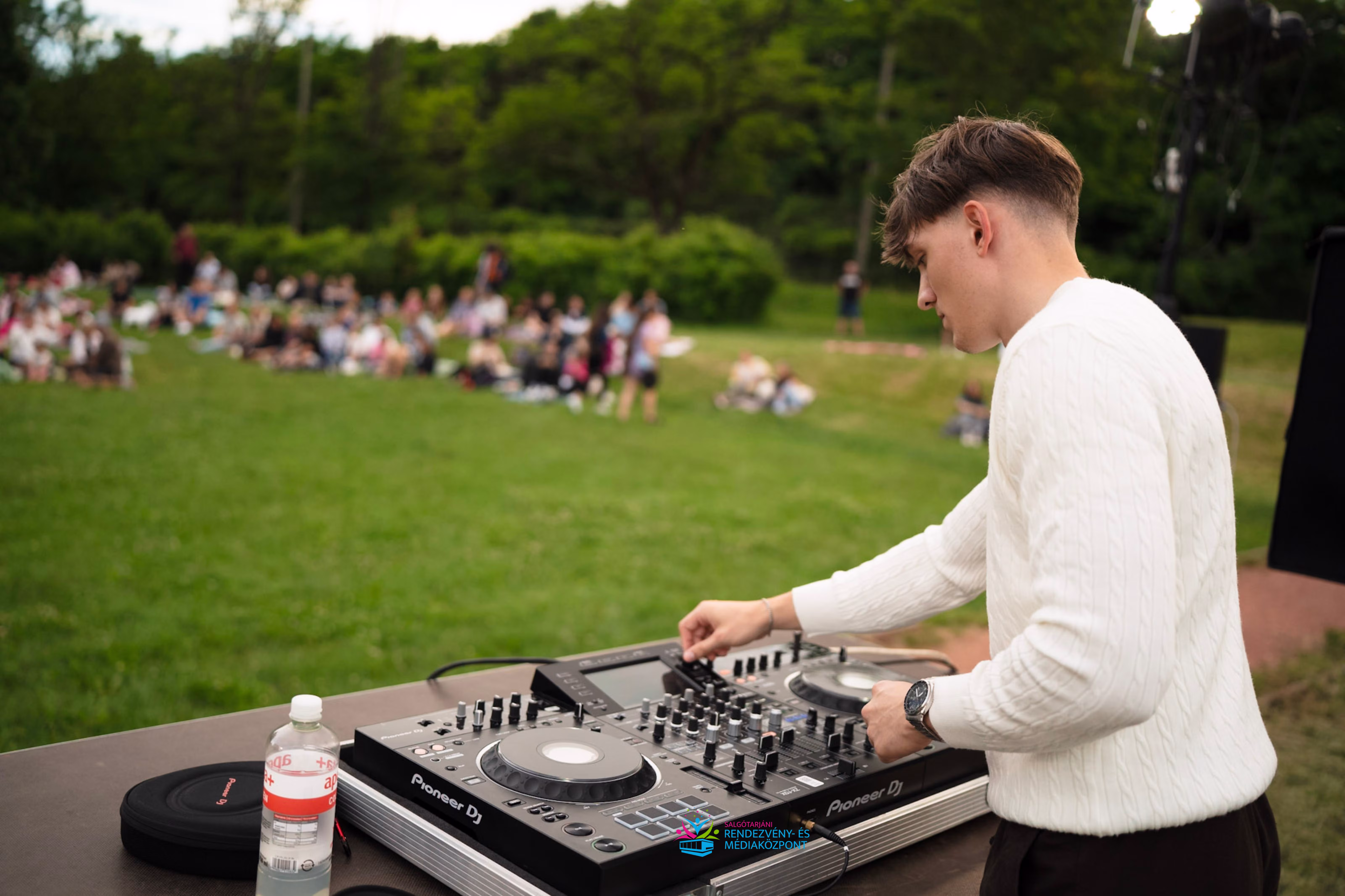 Közeli kép DJ Balmierről, miközben az Összetartozás Pikniken zenél, a háttérben a közönséggel.